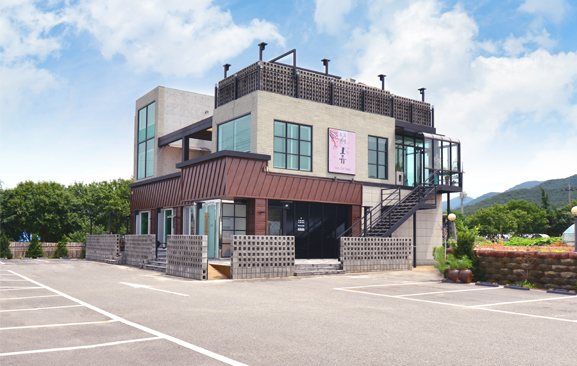파란 하늘 아래 도고휴펜션 건물과 넓은 주차장(낮)